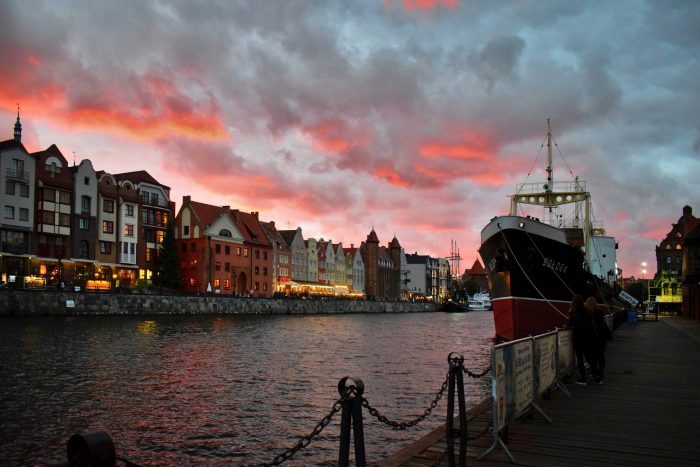 A ship moored and standing still at the dock in Gdańsk harbor, with historic buildings visible in the background
