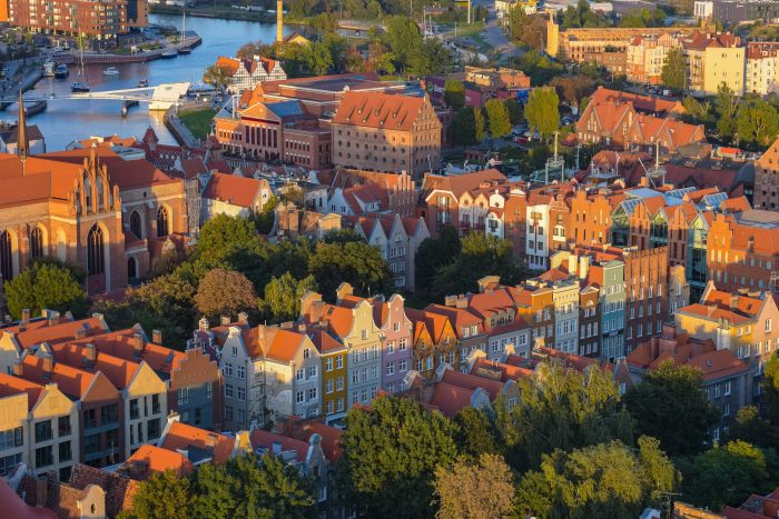 A panoramic view of Gdańsk’s historic Old Town with colorful buildings along the Motława River and ships docked at the harbor
