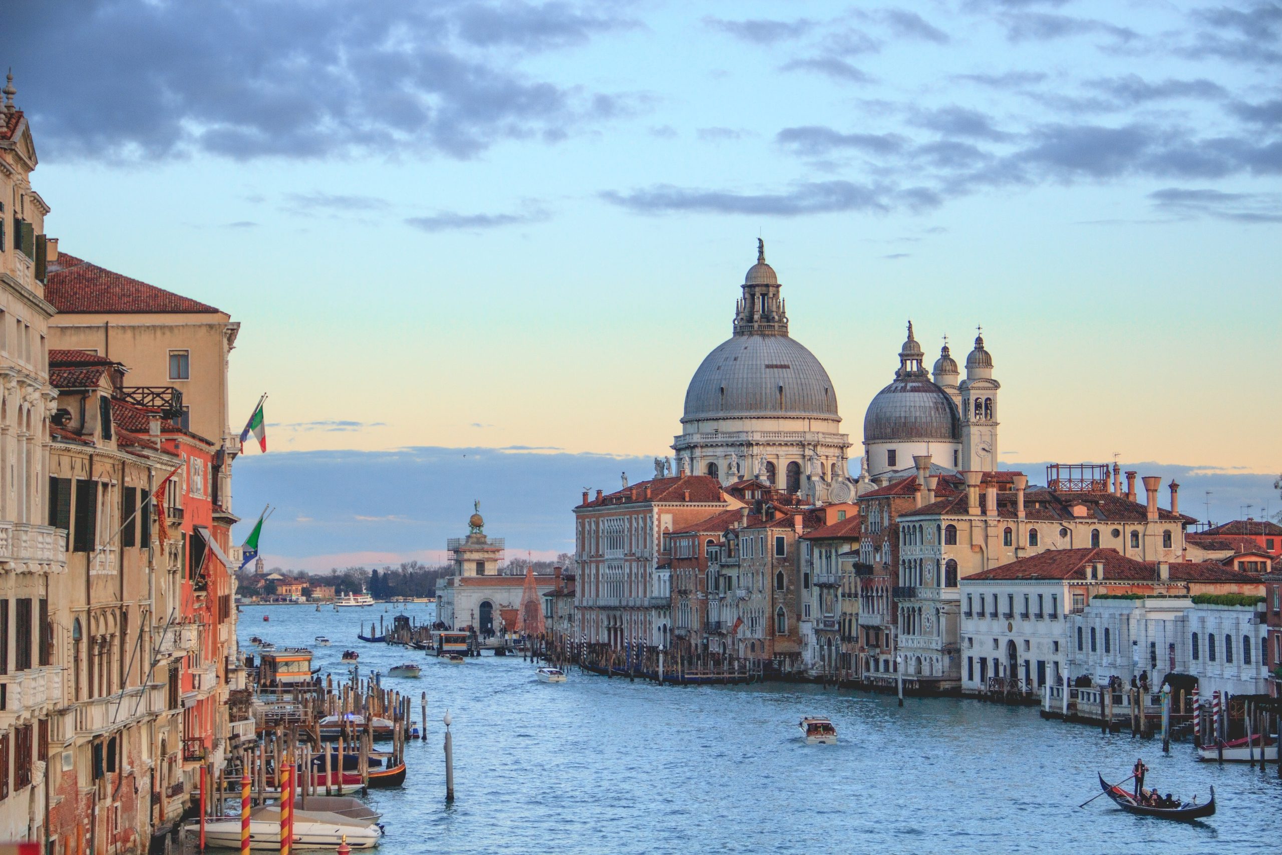 A panoramic luxury view of Venice’s winding canals with historic buildings and boats under a clear sky. contact us now